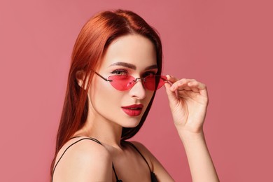 Photo of Beautiful woman with red dyed hair and sunglasses on pink background