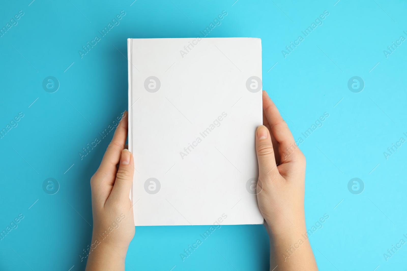Photo of Woman holding book with blank cover on blue background, top view