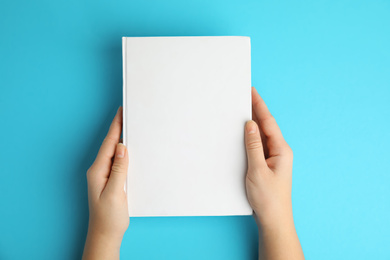 Photo of Woman holding book with blank cover on blue background, top view