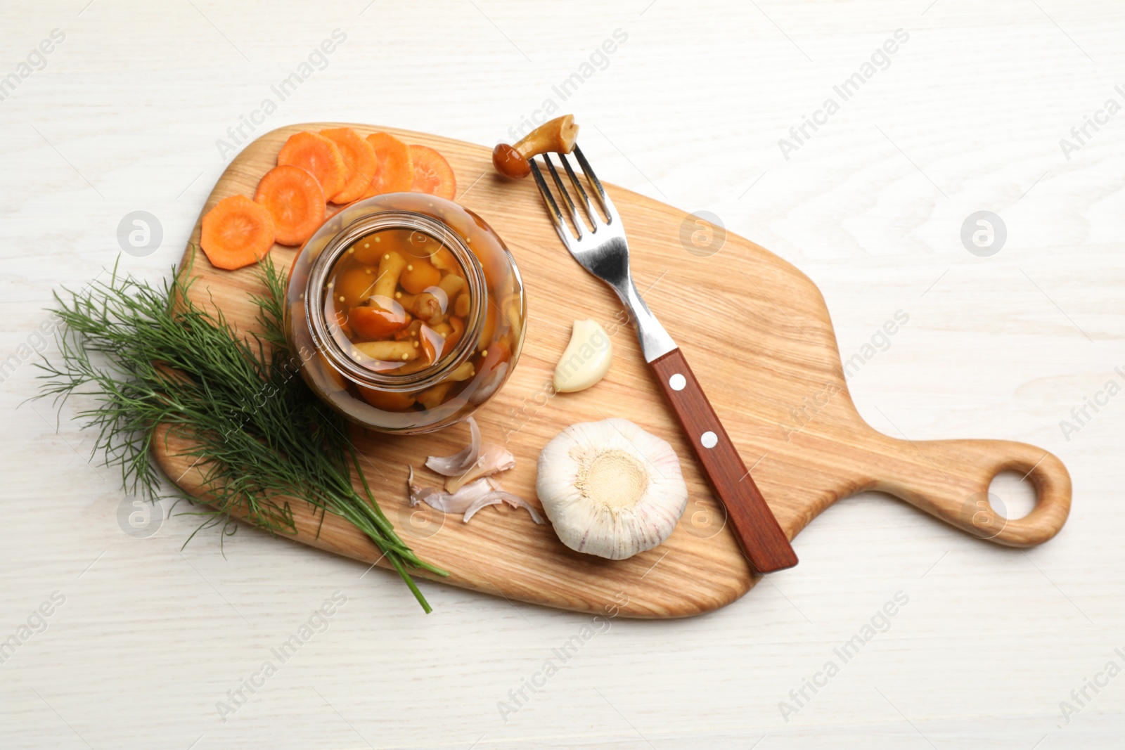 Photo of Delicious marinated mushrooms in glass jar and ingredients on white wooden table, flat lay