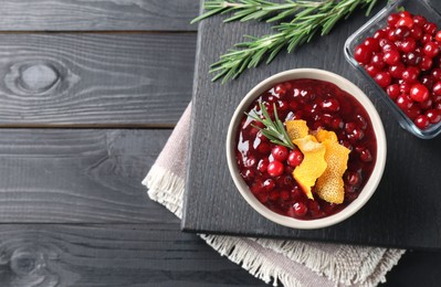 Photo of Fresh cranberry sauce, rosemary, orange peel and berries on black wooden table, top view. Space for text