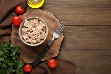 Bowl with canned tuna and products on wooden table, flat lay. Space for text