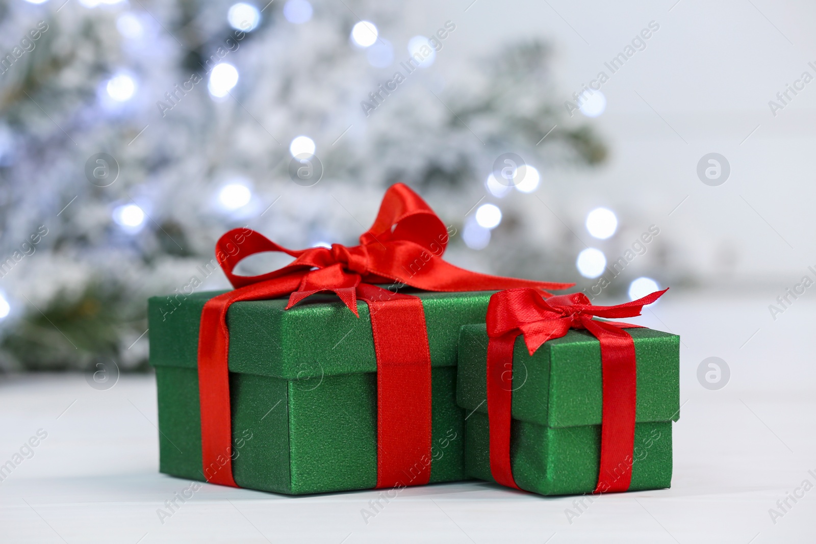 Photo of Beautiful gift boxes on white table against blurred festive lights. Christmas present