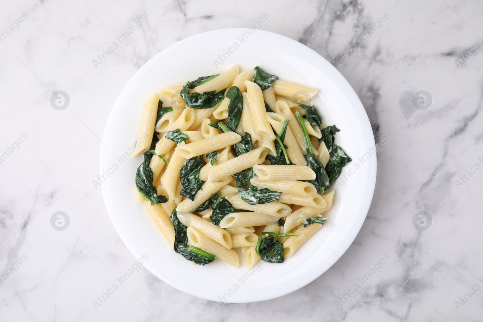 Photo of Tasty pasta with spinach and sauce on white marble table, top view