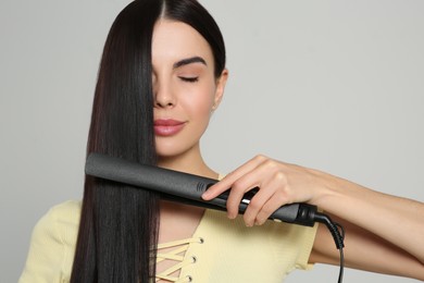 Photo of Beautiful woman using hair iron on light grey background