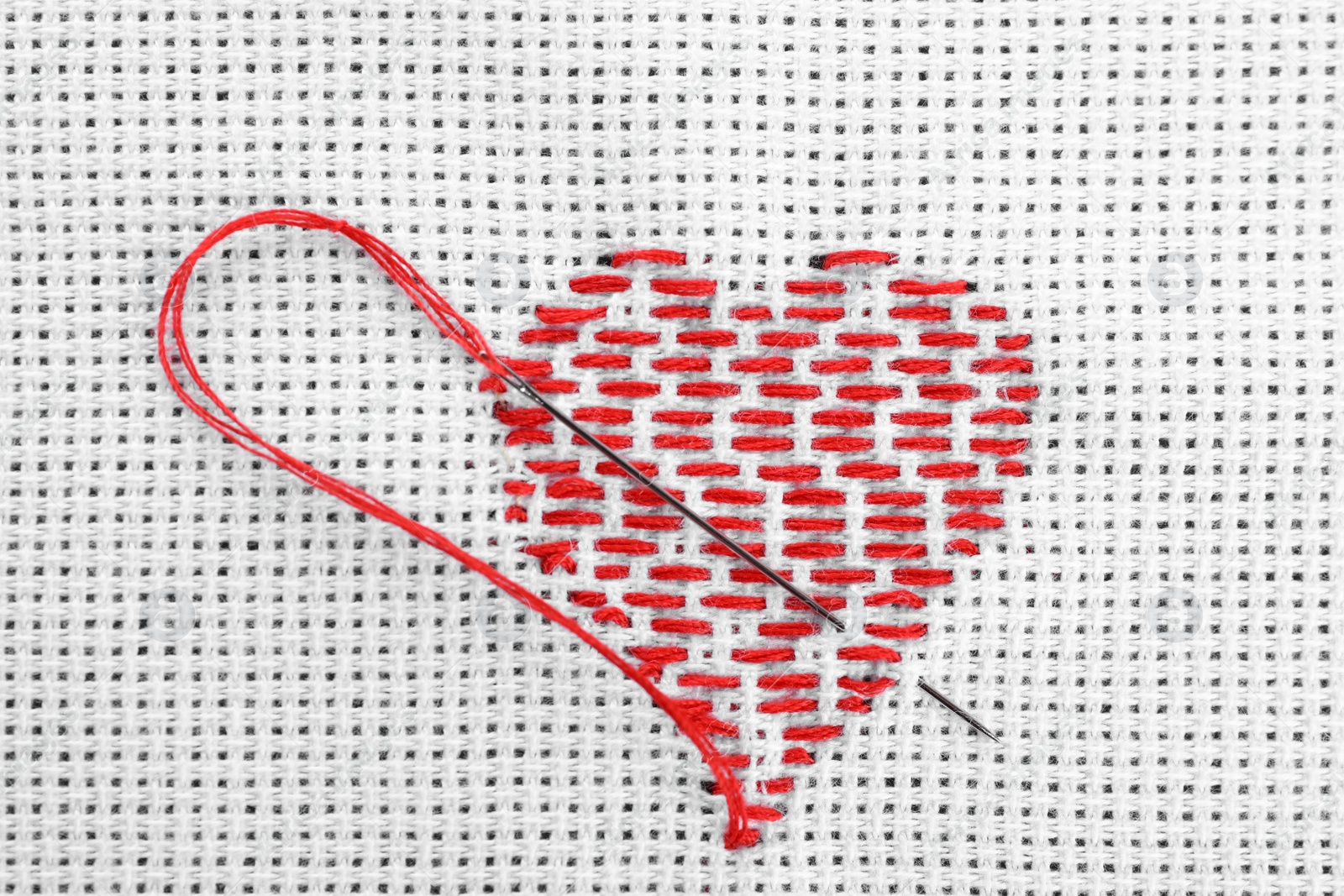 Photo of Canvas with embroidered heart and needle as background, top view