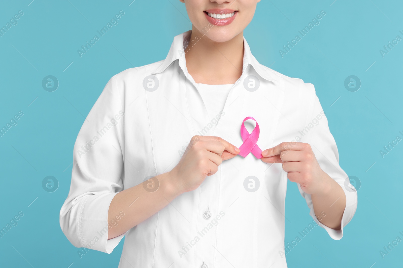 Photo of Mammologist with pink ribbon on light blue background, closeup. Breast cancer awareness