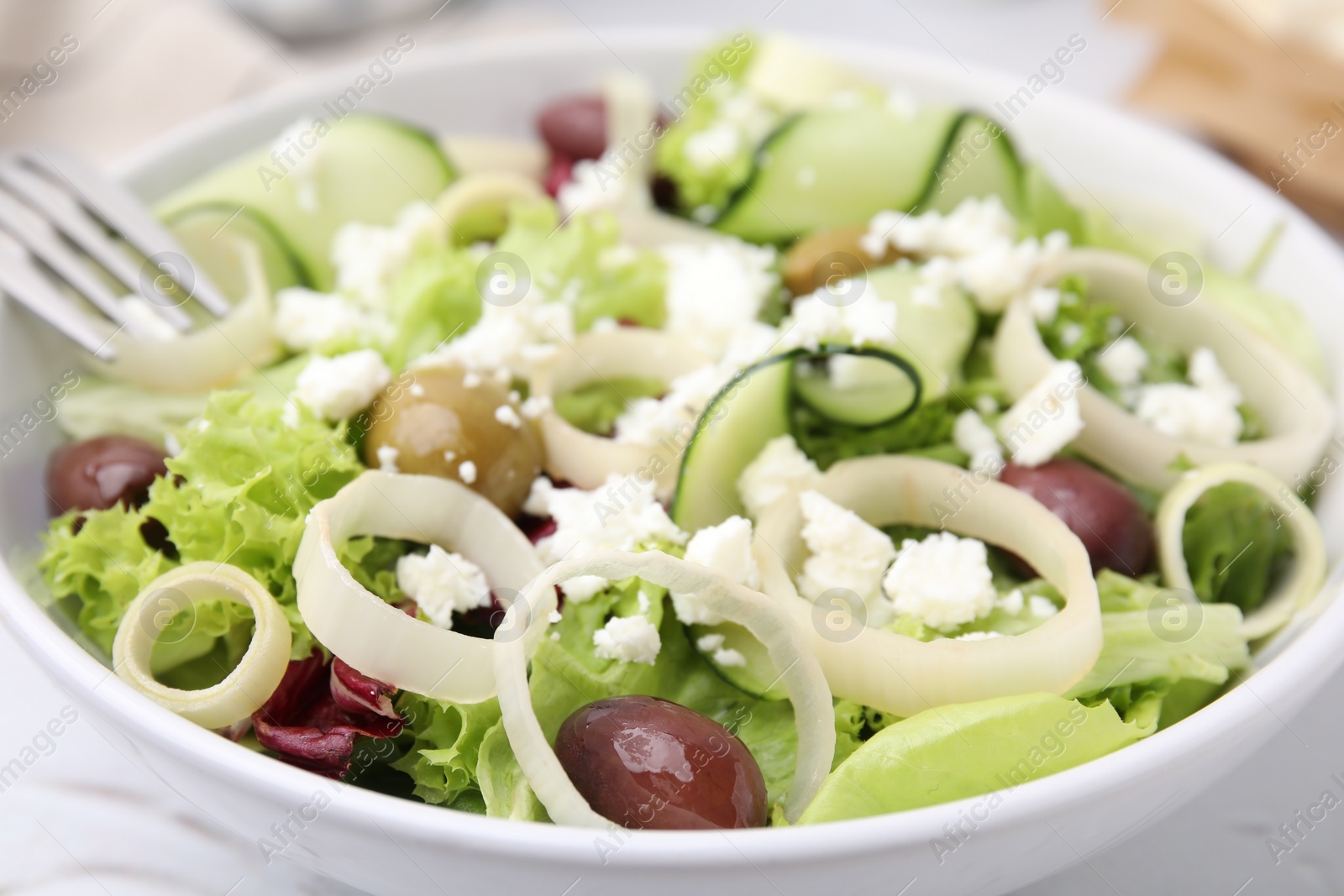 Photo of Bowl of tasty salad with leek, olives and cheese on white table, closeup