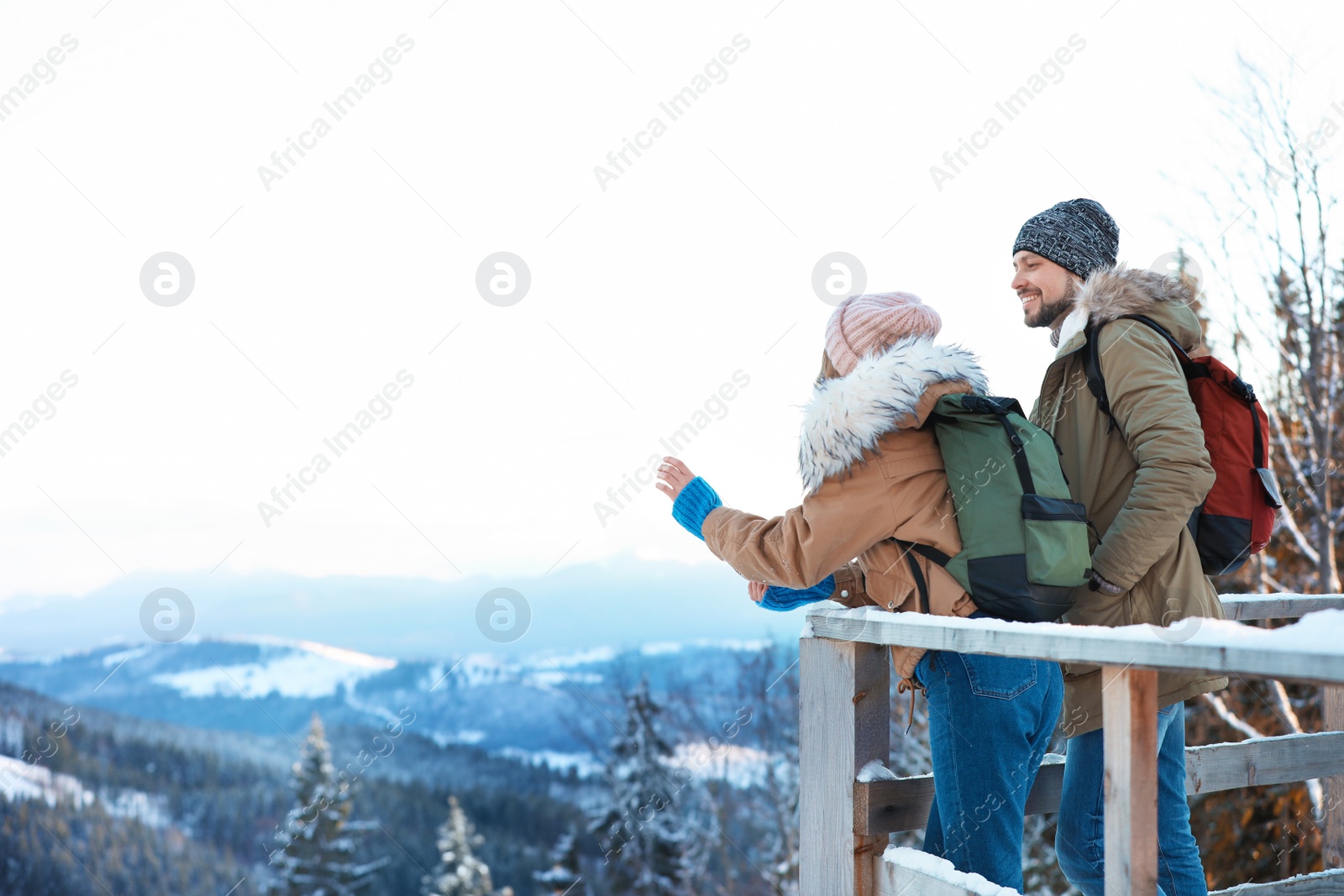 Photo of Couple with backpacks enjoying mountain view during winter vacation. Space for text