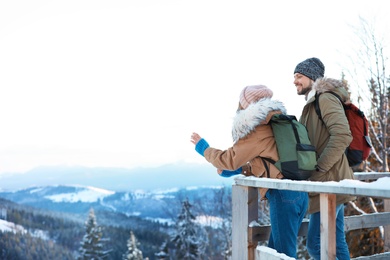 Couple with backpacks enjoying mountain view during winter vacation. Space for text