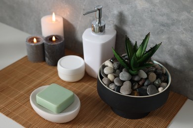Potted artificial plant, soap, burning candles and bamboo mat on white table
