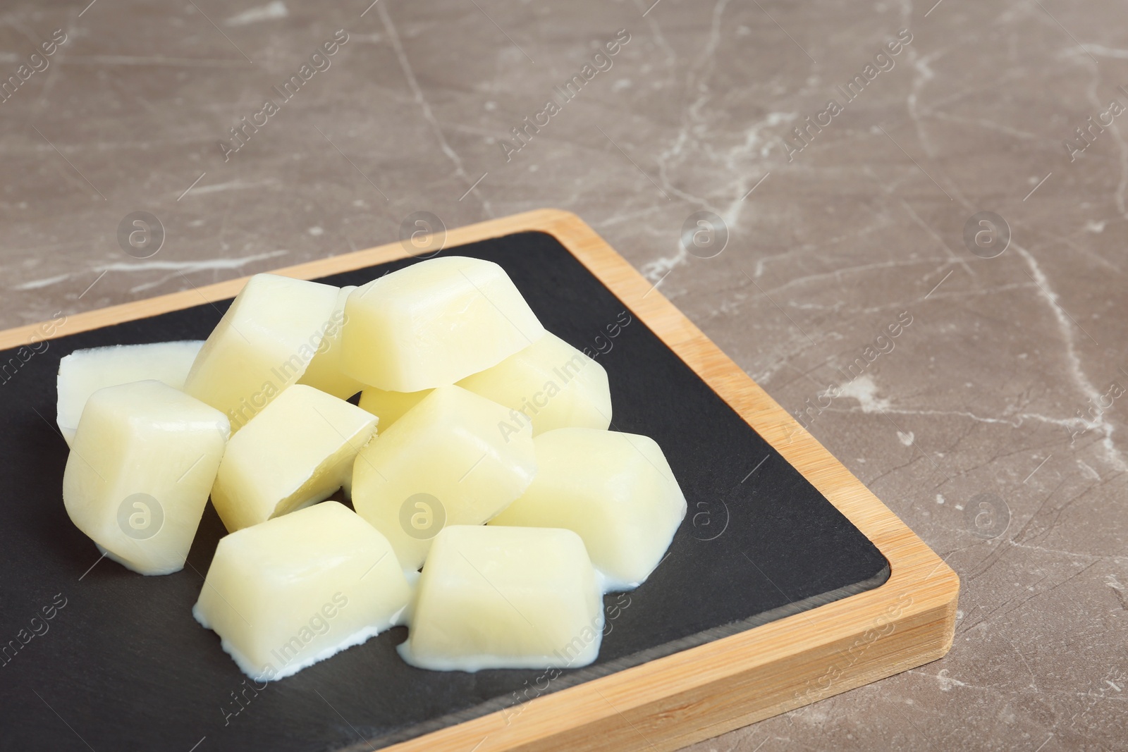 Photo of Board with milk ice cubes on grey table. Space for text