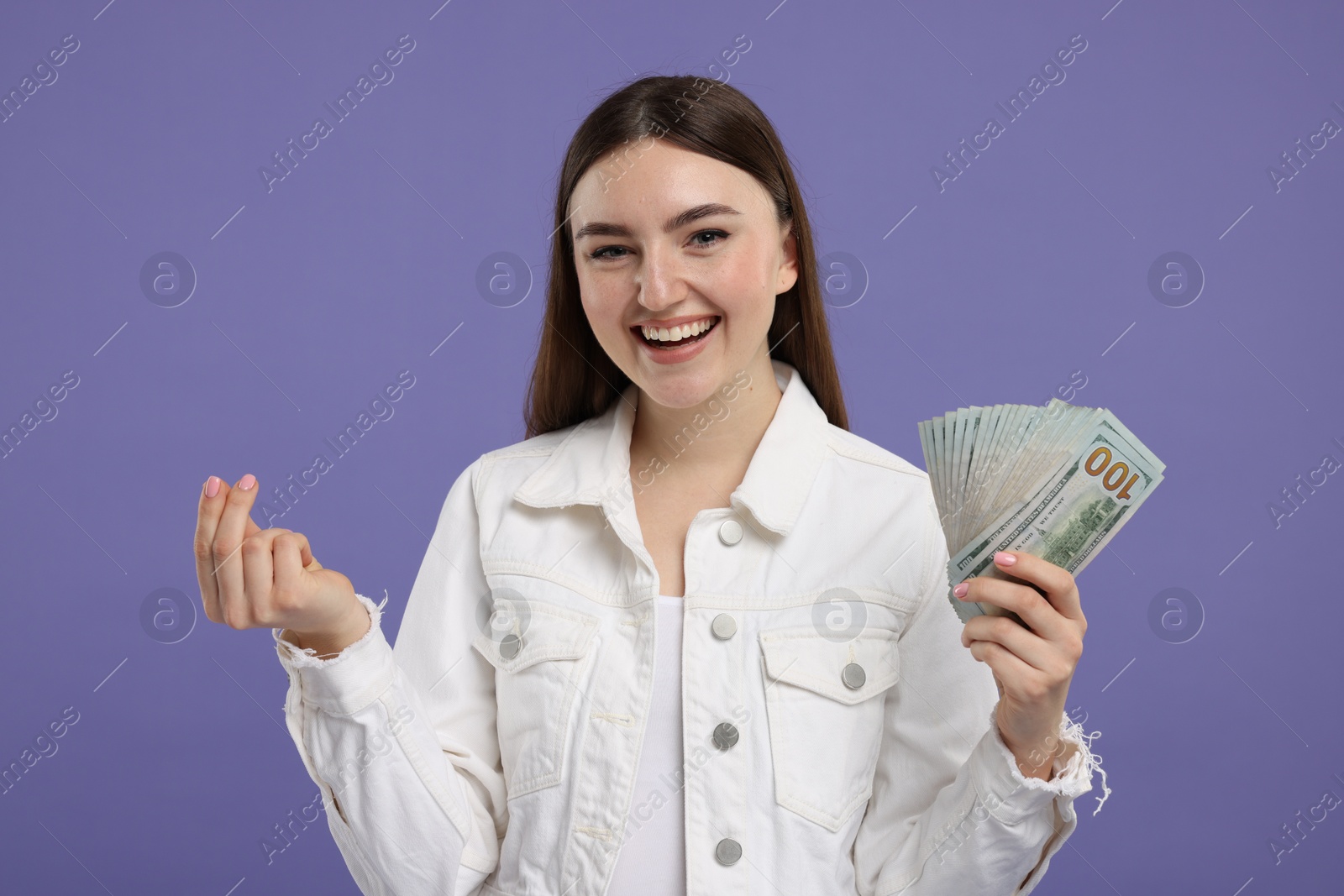 Photo of Happy woman with dollar banknotes showing money gesture on purple background