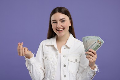 Photo of Happy woman with dollar banknotes showing money gesture on purple background