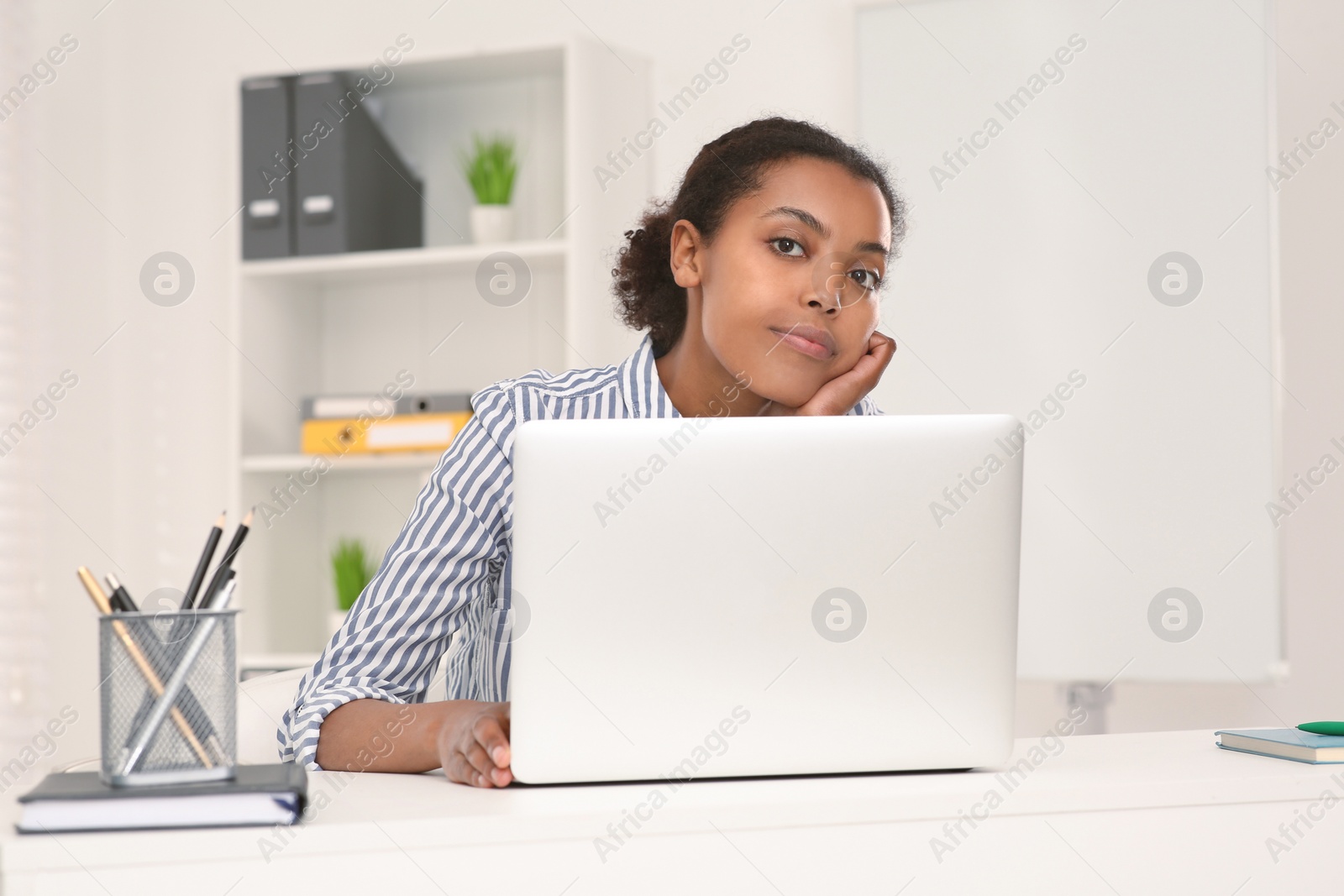 Photo of Sad African American intern working on laptop at white table in office. First work day
