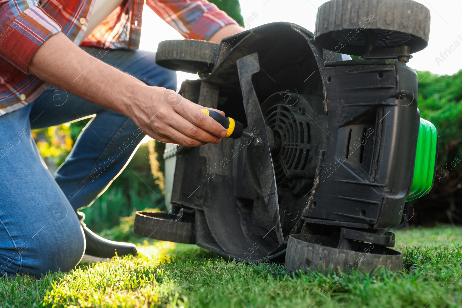Photo of Man with screwdriver fixing lawn mower outdoors, closeup