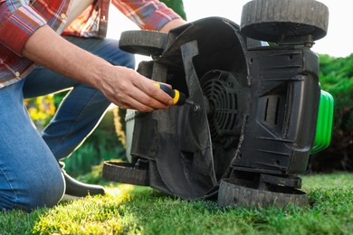 Photo of Man with screwdriver fixing lawn mower outdoors, closeup