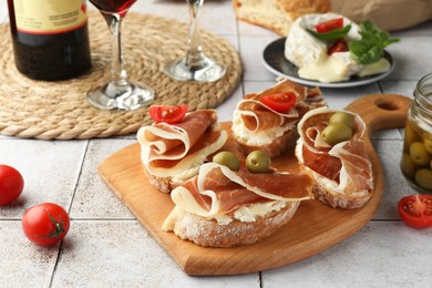 Photo of Tasty sandwiches with cured ham, tomatoes and olives on tiled table