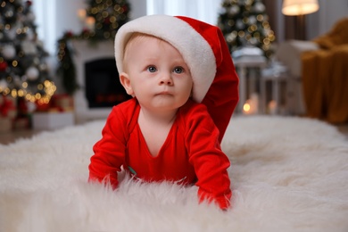 Photo of Cute little baby in red bodysuit and Santa hat on floor at home. Christmas suit