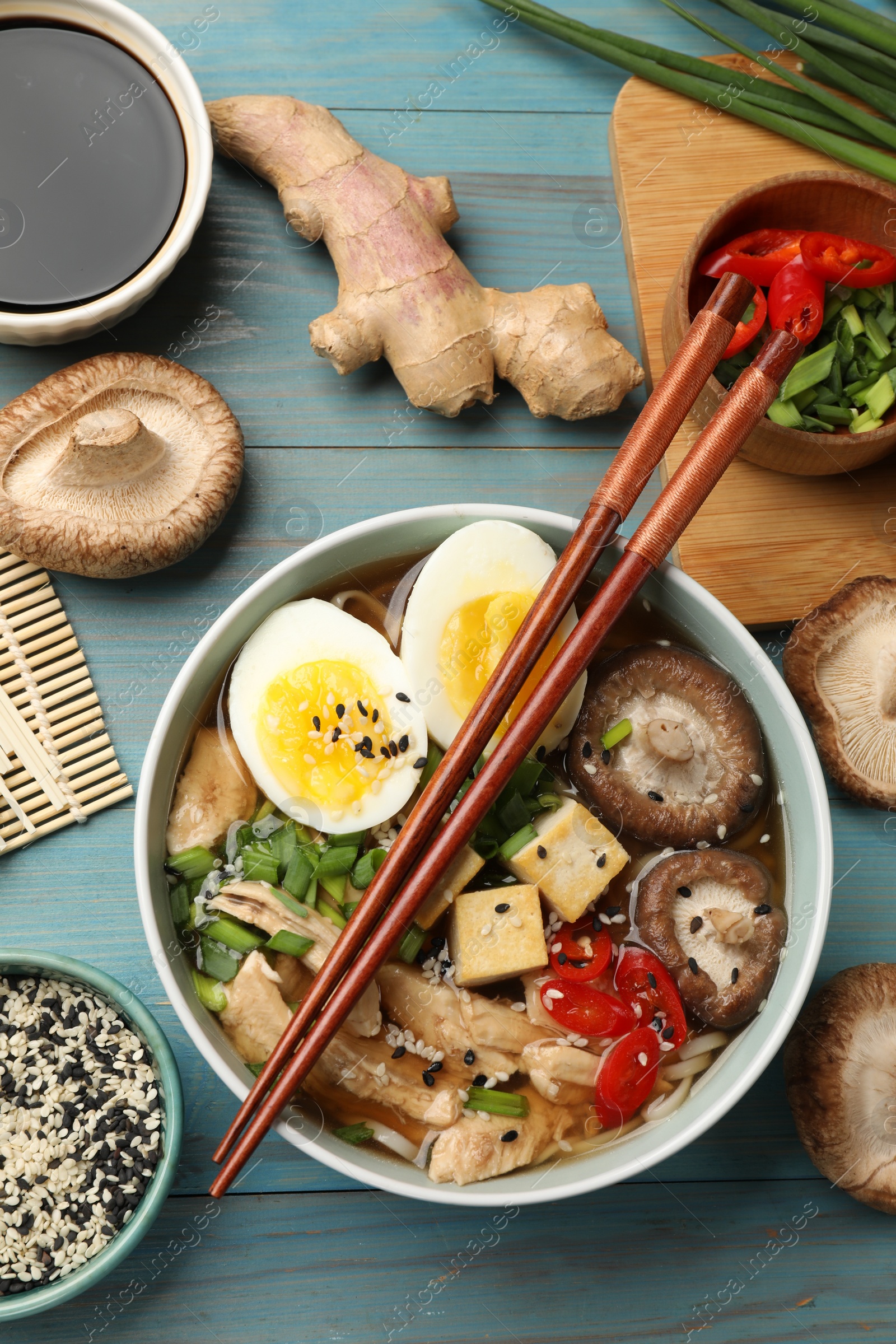 Photo of Bowl of delicious ramen and ingredients on light blue wooden table, flat lay. Noodle soup