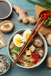 Photo of Bowl of delicious ramen and ingredients on light blue wooden table, flat lay. Noodle soup