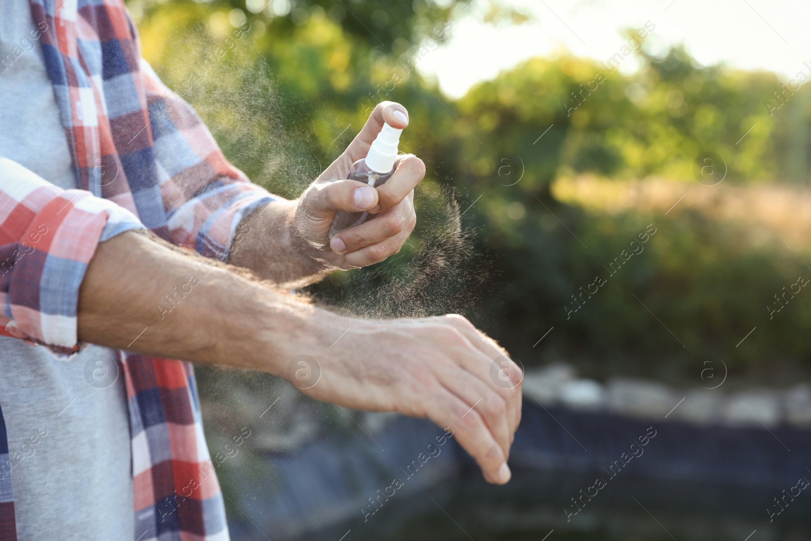 Photo of Man applying insect repellent onto hand outdoors, closeup