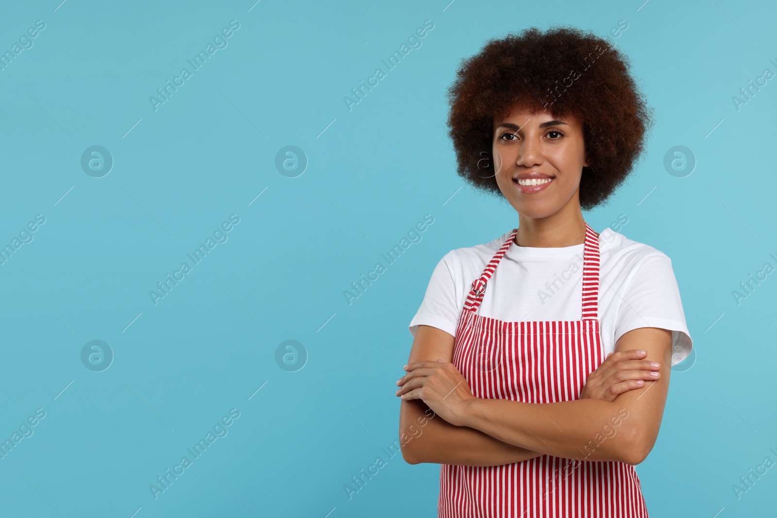 Photo of Portrait of happy young woman in apron on light blue background. Space for text