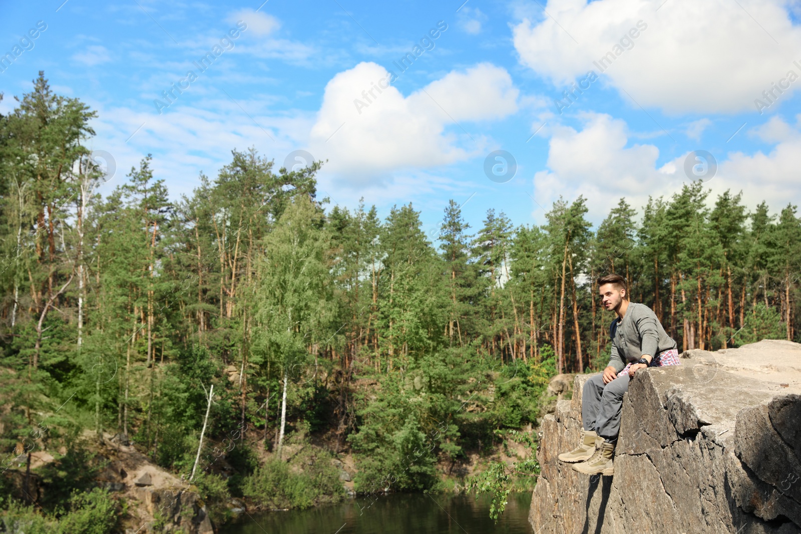 Photo of Young man on rock near lake and forest. Camping season