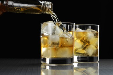 Pouring tasty whiskey from bottle into glass at mirror table, closeup