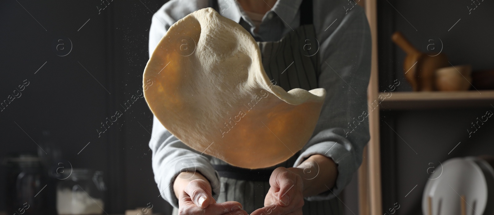 Photo of Woman tossing pizza dough in kitchen, closeup