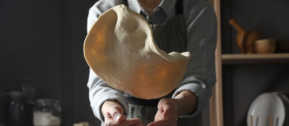 Photo of Woman tossing pizza dough in kitchen, closeup