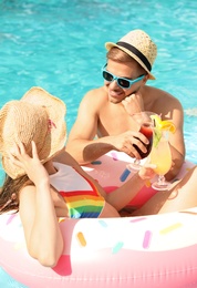 Young couple with cocktails in pool on sunny day