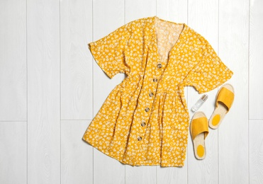 Stylish yellow dress, perfume and shoes on wooden floor, flat lay