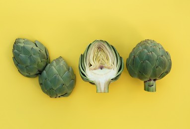 Photo of Whole and cut fresh raw artichokes on pale yellow background, flat lay