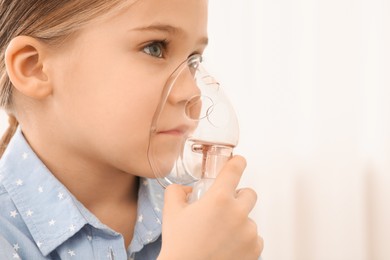 Photo of Sick little girl using nebulizer for inhalation indoors, closeup