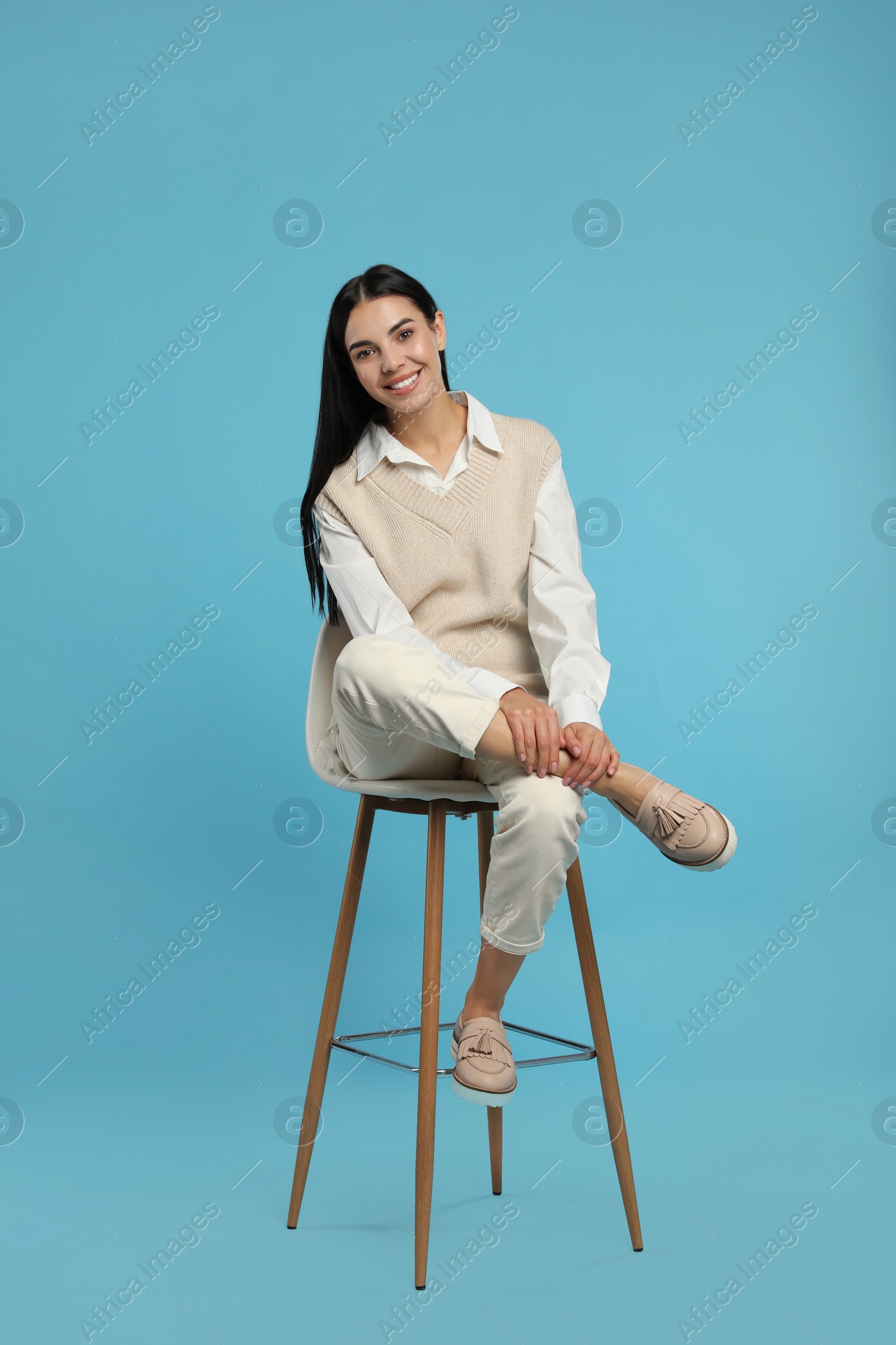 Photo of Beautiful young woman sitting on stool against turquoise background