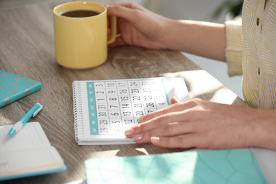 Photo of Woman with calendar and cup of drink at wooden table, closeup