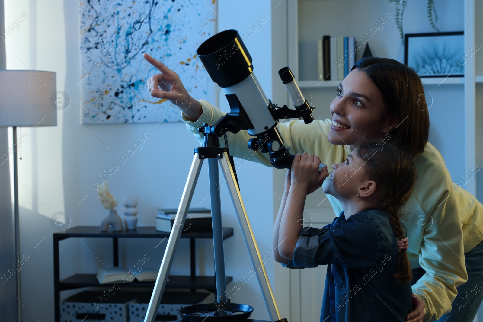 Photo of Happy mother and her cute daughter using telescope to look at stars in room