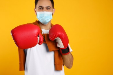 Photo of Man with protective mask and boxing gloves on yellow background, space for text. Strong immunity concept
