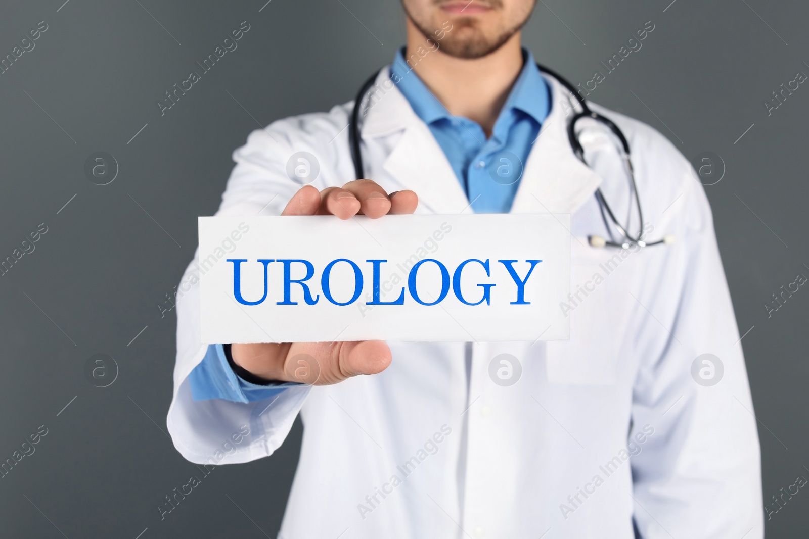 Photo of Male doctor holding paper with word UROLOGY on grey background