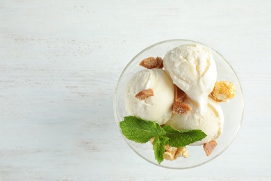 Photo of Delicious ice cream with caramel candies and popcorn in dessert bowl on white wooden table, top view. Space for text