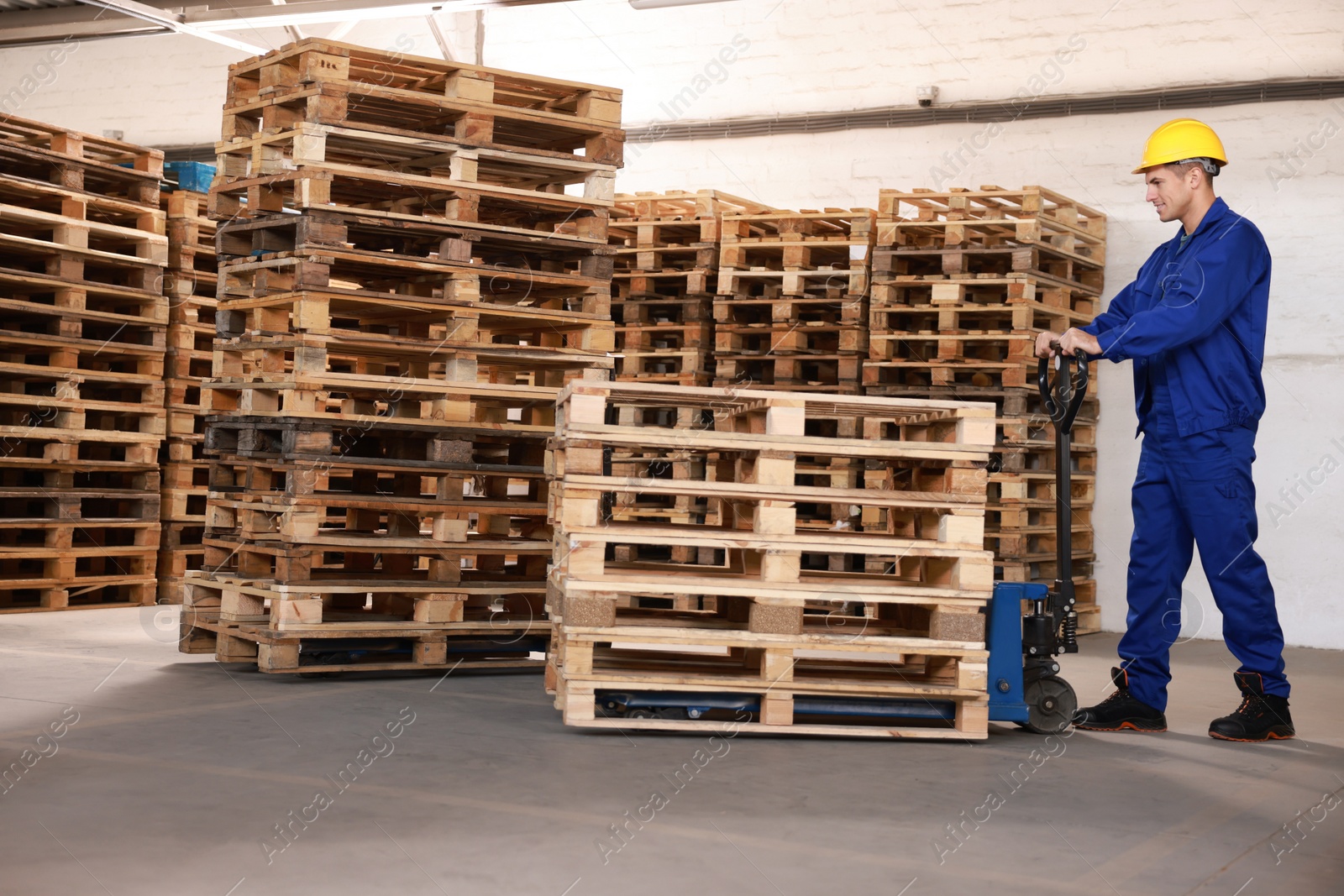 Image of Worker moving wooden pallets with manual forklift in warehouse