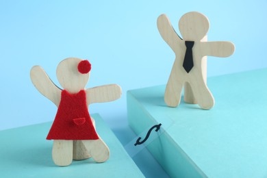 Photo of Gender pay gap. Wooden figures of man and woman on light blue background