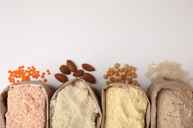 Photo of Paper bags with different types of flour on white background, top view. Space for text