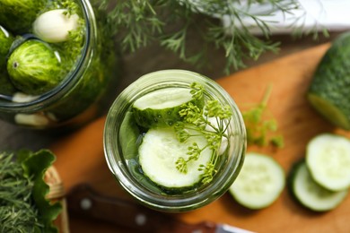 Photo of Glass jars, fresh cucumbers and herbs on wooden table, closeup. Pickling recipe