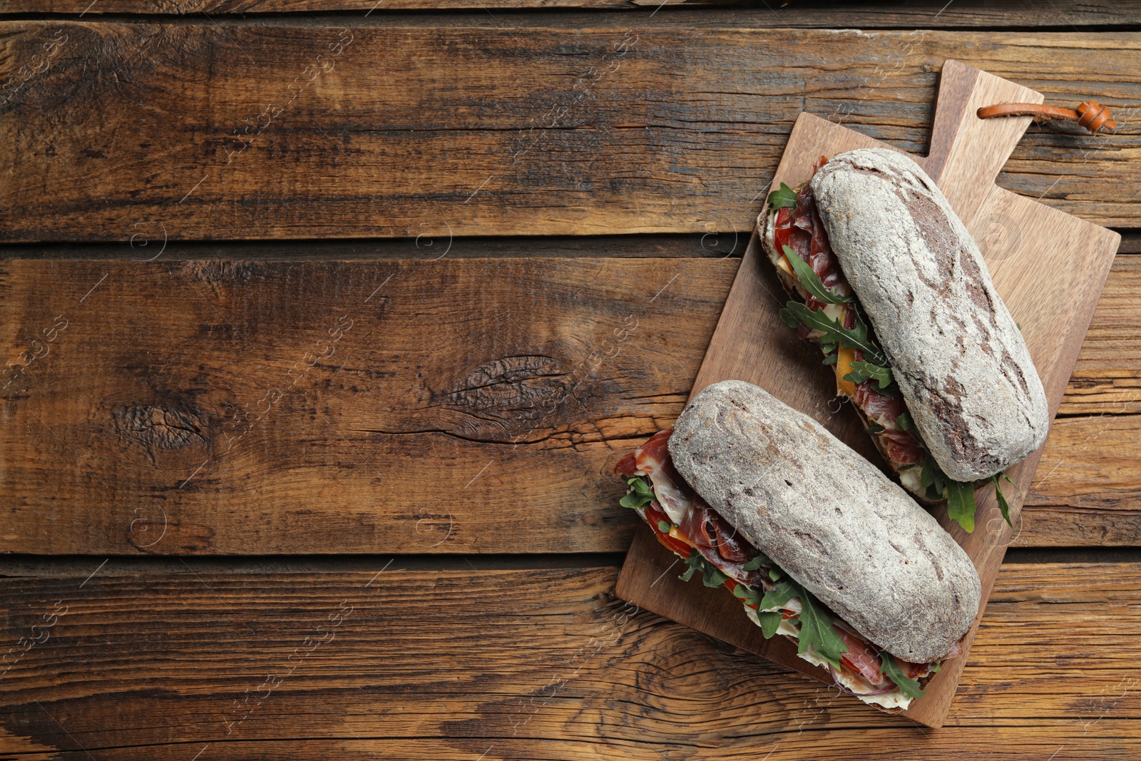 Photo of Delicious sandwiches with fresh vegetables and prosciutto on wooden table, top view. Space for text