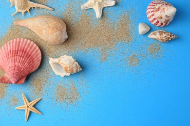 Photo of Beautiful starfishes, shells and sand on blue background, flat lay. Space for text