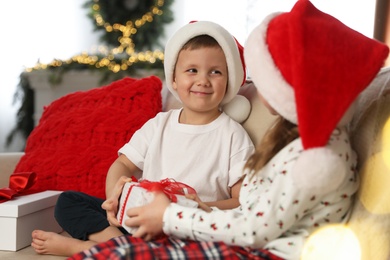 Photo of Cute children holding gift box on sofa in room decorated for Christmas
