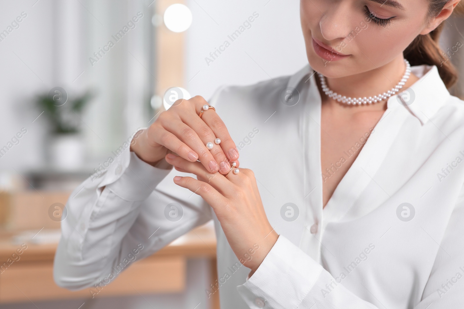 Photo of Young woman trying on elegant rings with pearls indoors, closeup