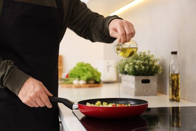 Photo of Cooking process. Man pouring oil into frying pan in kitchen, closeup